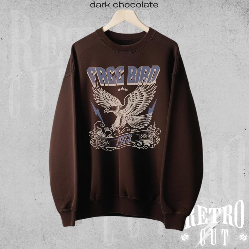 May include: A dark brown sweatshirt with a vintage-style graphic of a flying eagle with the text "FREE BIRD 1973" printed on the front.