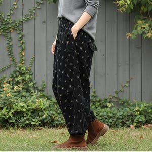 May include: Black corduroy pants with a floral pattern. The pants have pockets and are worn with brown boots and a gray long-sleeve shirt. The pants are loose-fitting and appear comfortable.