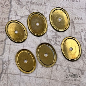 May include: Six oval-shaped brass metal blanks with a small hole in the center. The blanks are smooth and have a shiny finish.