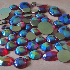May include: A collection of ruby red and blue iridescent glass rhinestones. The rhinestones are various shapes and sizes, including round, oval, and square.
