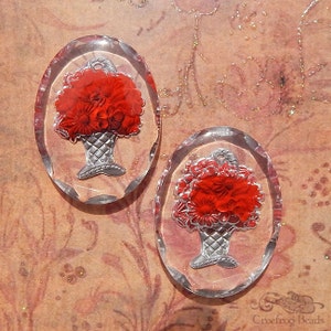 May include: Two oval-shaped glass cabochons with a red floral design in a silver basket. The cabochons are clear and have a slightly textured surface.
