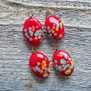 4 Vintage Japanese Tombo glass pendants with millefiori flower design on bright red. 15x21 mm puffy oval drops or charms w/ gold toned loop.