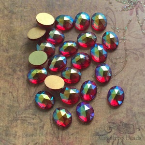 May include: A collection of 20 red oval-shaped iridescent glass rhinestones. The rhinestones have a faceted design and a rainbow-like sheen.