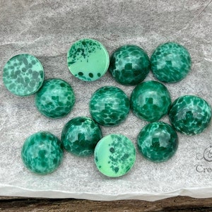 May include: A collection of 12 green and white glass cabochons with a marbled pattern. The cabochons are round and have a smooth, glossy finish.