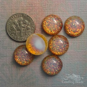 Op de afbeelding: Zes ronde, iriserende, oranje en gouden glitter cabochons. De cabochons zijn ongeveer 2,5 cm in diameter.