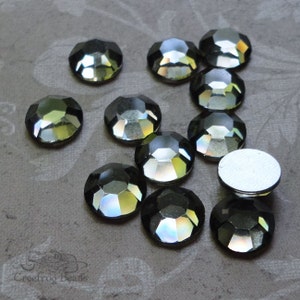 May include: A close-up of a group of 10 iridescent black rhinestones. The rhinestones are faceted and have a reflective surface. They are arranged in a random pattern on a gray background.
