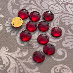 Puede incluir: Un grupo de 12 piedras de cristal rojas de coser con dos agujeros. Las piedras de cristal son redondas y tienen un diseño facetado.