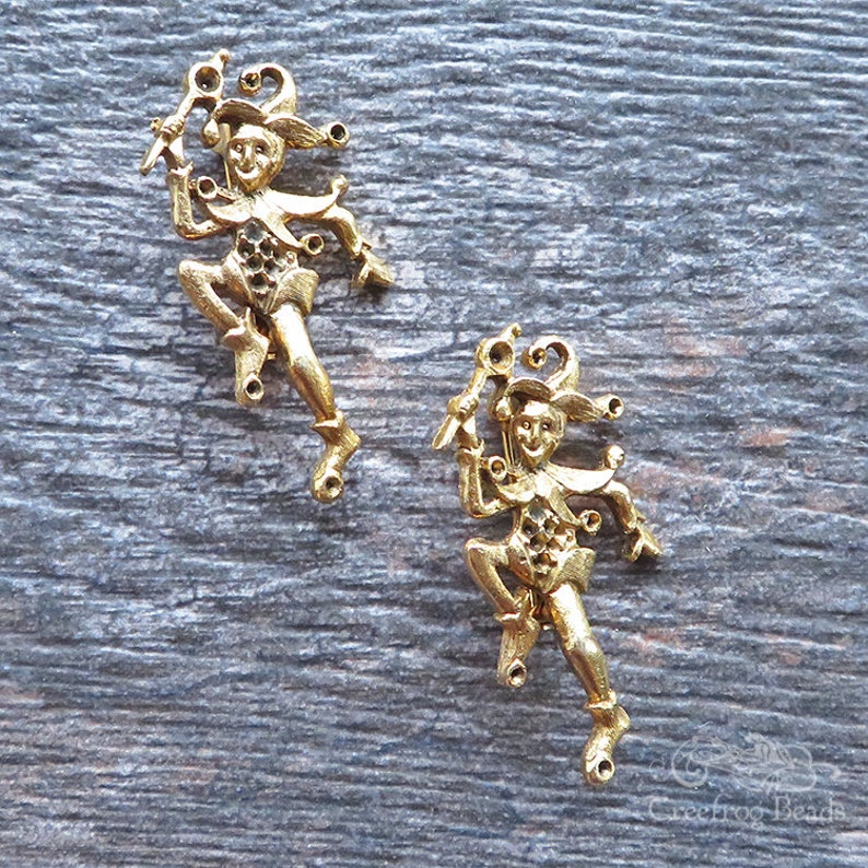 May include: Two gold-tone metal jester figurines with a whimsical design. Each jester is holding a staff and has a jester hat with bells.