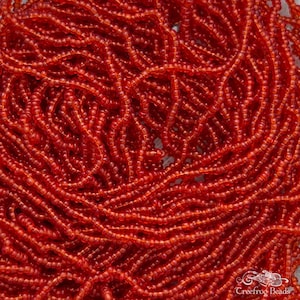 May include: A close-up image of a pile of small, round, orange glass beads. The beads are arranged in a random pattern and are all the same size.