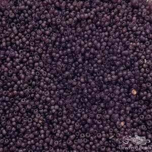 May include: A close-up view of a large quantity of small, round, opaque purple glass beads. The beads are all approximately the same size and shape, and they are arranged in a random pattern.
