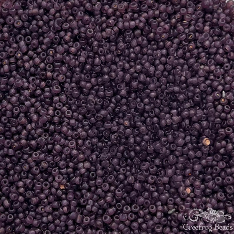 May include: A close-up view of a large quantity of small, round, opaque purple glass beads. The beads are all approximately the same size and shape, and they are arranged in a random pattern.