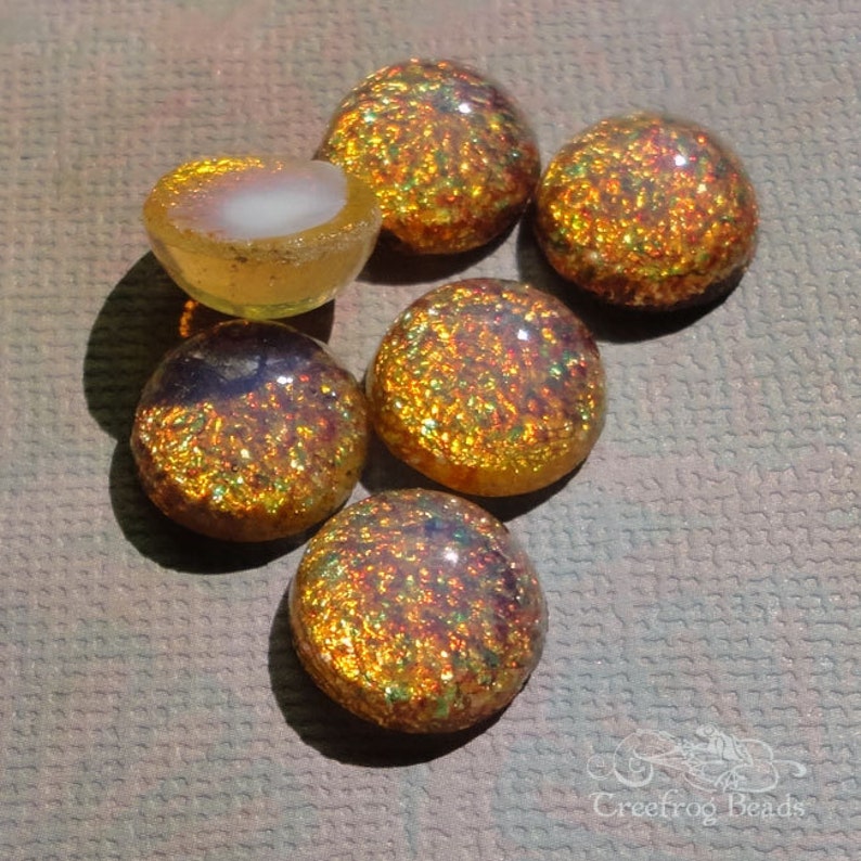 Op de afbeelding: Zes iriserende glazen cabochons in tinten van goud, oranje en groen. De cabochons hebben een getextureerd oppervlak en zijn perfect voor het maken van sieraden.