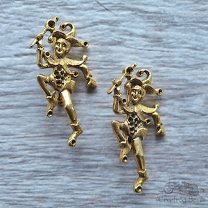 May include: Two gold-tone metal jester figurines with a whimsical design. Each jester is holding a staff and has a playful expression.