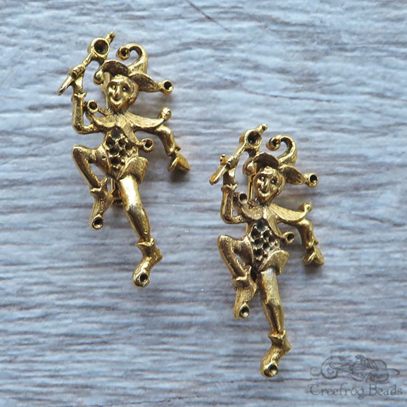 May include: Two gold-tone metal jester figurines with a whimsical design. Each jester is holding a staff and has a playful expression.