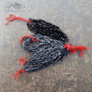 May include: Two strands of black glass beads, one strand is a darker black and the other is a lighter gray. Both strands have red string ties.