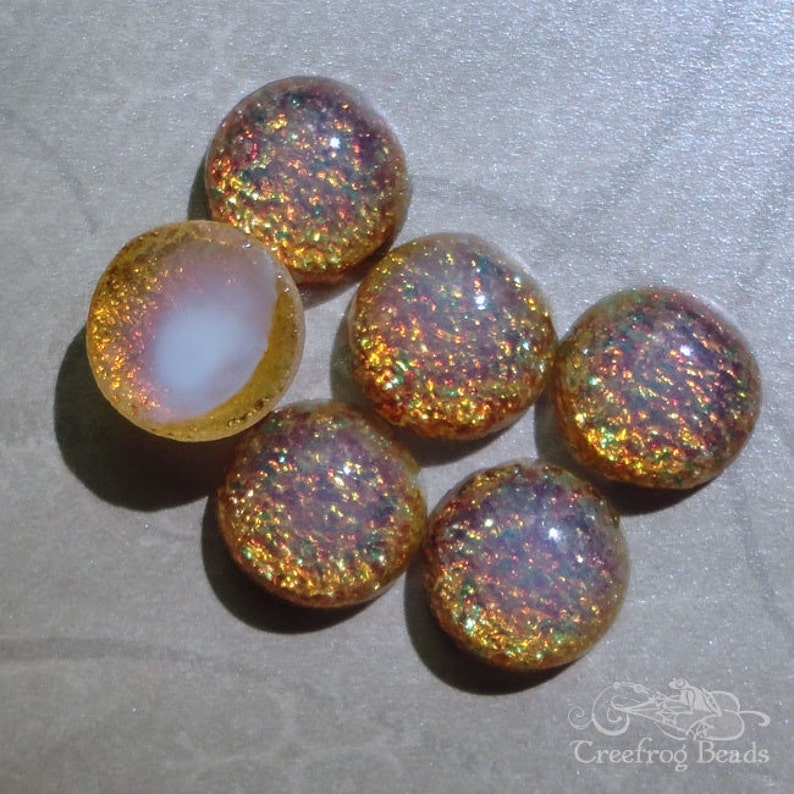 Op de afbeelding: Zes iriserende glazen cabochons in tinten van goud, roze en wit. De cabochons hebben een getextureerd oppervlak en zijn perfect voor het maken van sieraden.