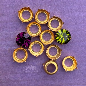 以下が含まれることがあります： 画像の中央に、紫色のラインストーンと緑色のラインストーンが1つずつある、金色の金属製のラインストーンセッティングのグループ。セッティングは、底に4つの爪があります。