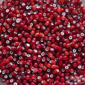 May include: A close-up of a large quantity of small, red and white glass beads. The beads are round and have a white ring around the centre.
