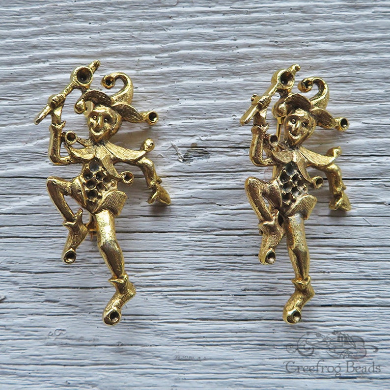 May include: Two gold-toned metal jester figurines with a whimsical design. Each jester is holding a staff and has a bell on their hat.