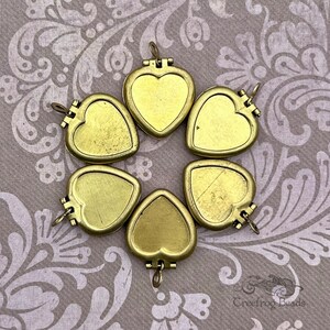 May include: Six gold-toned heart-shaped locket pendants with hinged lids. The lockets are arranged in a circle on a patterned background.