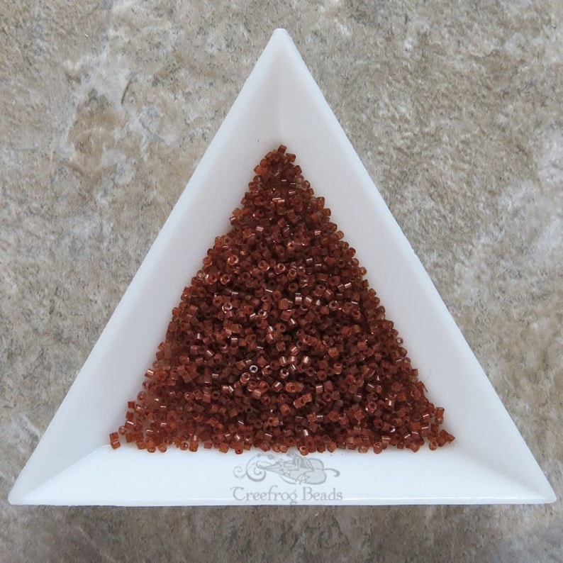 May include: A triangular white dish filled with a large pile of small, brown seed beads.