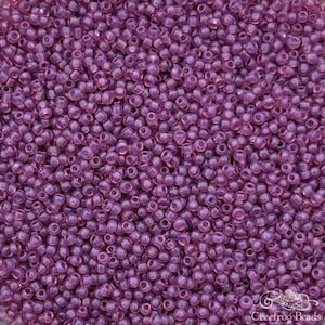 May include: A close-up view of a large quantity of small, round, translucent purple beads. The beads are opaque and have a slight sheen.