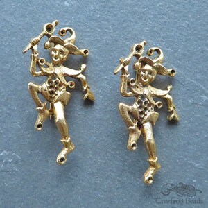 May include: Two gold-tone metal jester figurines with a whimsical design. Each jester is holding a staff and has a jester hat with bells.