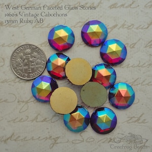 May include: A collection of 13mm ruby red faceted glass cabochons with an iridescent finish. The stones are vintage and from West Germany. The cabochons are displayed on a white surface with a US dime for scale.