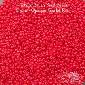 May include: A close-up view of a pile of small, opaque scarlet red seed beads. The beads are vintage Italian and size 11.