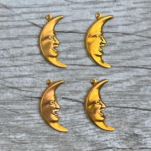 May include: Four gold-toned metal crescent moon charms with a face on each side. The charms are on a wooden surface.