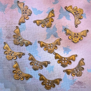May include: Twelve antique gold-toned metal embellishments with a decorative wheel design. Each embellishment has a scalloped edge and two loops for attaching.