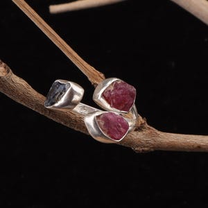 Könnte beinhalten: Ein Silberring mit drei rohen, ungeschliffenen Edelsteinen in Metallfassungen. Ein Stein ist dunkelgrau, während die anderen beiden tiefrot sind. Der Ring ist offen gestaltet und trägt einen kleinen 925-Stempel auf der Innenseite der Schiene.