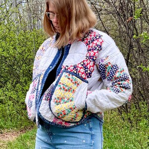 Peut inclure: Une veste matelassée fabriquée à partir de tissu blanc recyclé présentant des motifs patchwork floraux et géométriques colorés dans des tons de rouge, jaune et bleu, associée à un jean bleu clair orné de petites fleurs brodées blanches.