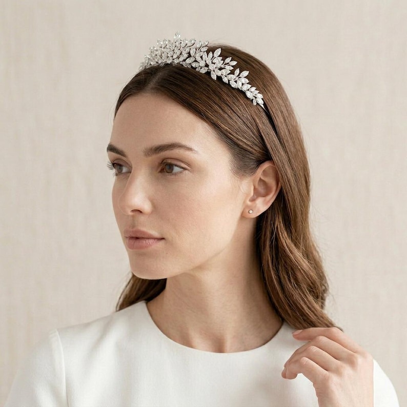 Elegant crystal bridal tiara with leaf-shaped rhinestones on silver headband. Sparkling wedding crown headpiece shown close-up, styled on bride hairstyle and displayed as bridal hair accessory for weddings.