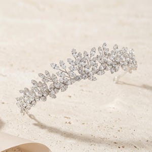 Elegant crystal bridal tiara with leaf-shaped rhinestones on silver headband. Sparkling wedding crown headpiece shown close-up, styled on bride hairstyle and displayed as bridal hair accessory for weddings.