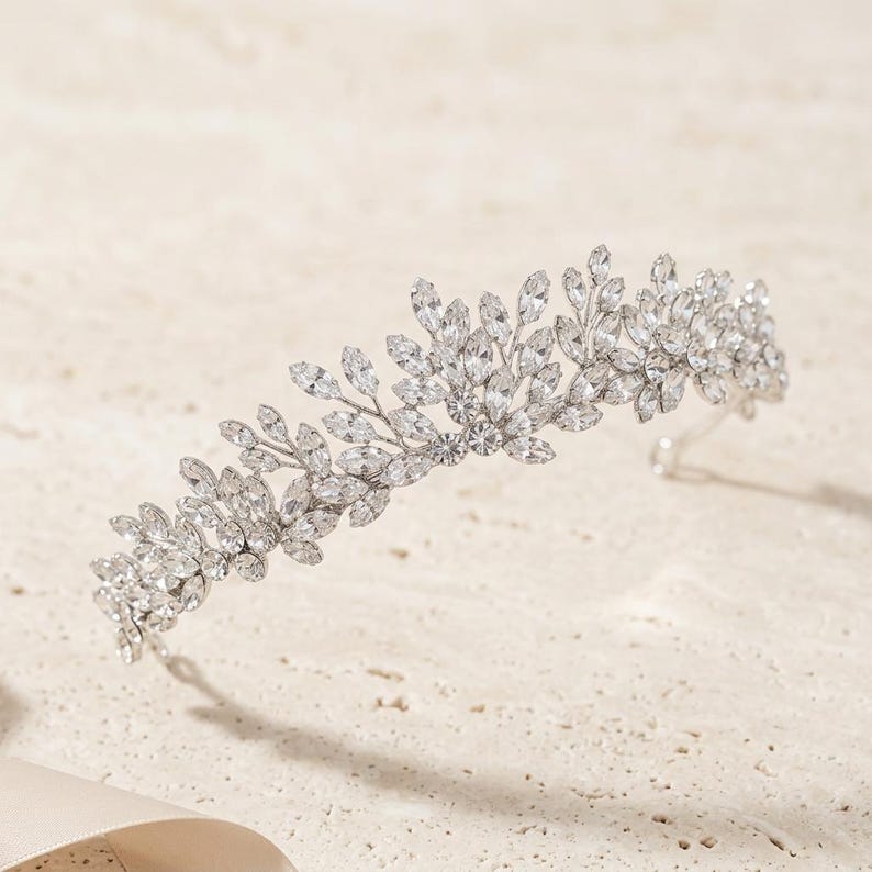 Elegant crystal bridal tiara with leaf-shaped rhinestones on silver headband. Sparkling wedding crown headpiece shown close-up, styled on bride hairstyle and displayed as bridal hair accessory for weddings.
