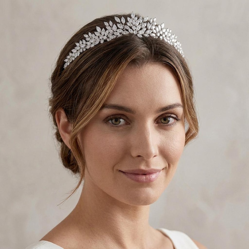 Elegant crystal bridal tiara with leaf-shaped rhinestones on silver headband. Sparkling wedding crown headpiece shown close-up, styled on bride hairstyle and displayed as bridal hair accessory for weddings.