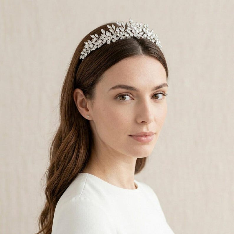 Elegant crystal bridal tiara with leaf-shaped rhinestones on silver headband. Sparkling wedding crown headpiece shown close-up, styled on bride hairstyle and displayed as bridal hair accessory for weddings.