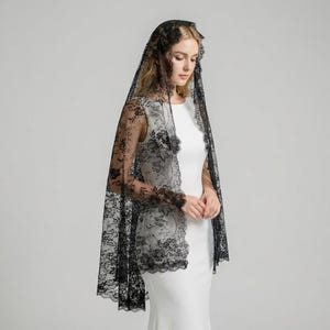 Könnte beinhalten: Ein schwarzer Spitzenschleier mit floralen Mustern. Der Schleier ist über Kopf und Schultern drapiert, wobei sich die Spitze über die Arme erstreckt. Das filigrane Design und der zarte Stoff erzeugen einen eleganten Look.