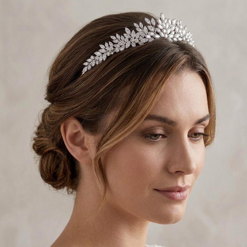 Elegant crystal bridal tiara with leaf-shaped rhinestones on silver headband. Sparkling wedding crown headpiece shown close-up, styled on bride hairstyle and displayed as bridal hair accessory for weddings.