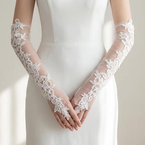 Könnte beinhalten: Elegante, lange weiße Spitzenhandschuhe mit floralen Mustern. Diese transparenten Handschuhe reichen über die Ellbogen und bieten einen zarten und raffinierten Look. Die aufwendigen Spitzendetails verleihen einen Hauch von Raffinesse, passend für Brautmode.