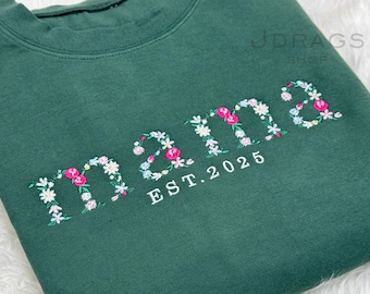 May include: A dark green sweatshirt with the word "mama" embroidered in floral letters. The embroidery includes pink and white flowers. Below the word "mama" is the text "EST. 2025" in white.