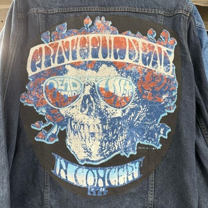 May include: A blue denim jacket with a black patch on the back. The patch features a skull with sunglasses and the text "Grateful Dead" and "In Concert 1974".