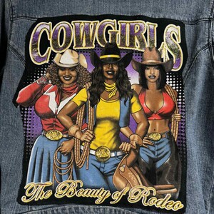 May include: A blue denim jacket with a black patch featuring three women wearing cowboy hats and the text "COWGIRLS The Beauty of Rodeo".