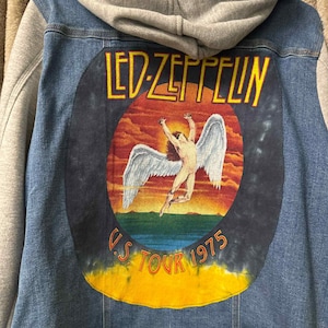 May include: A denim jacket with a gray hooded sweatshirt attached. The back of the jacket features a circular graphic with the words "LED ZEPPELIN" in yellow, and an image of a winged figure. The text "U.S. TOUR 1975" is also visible.