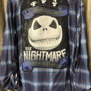 May include: A long-sleeved, button-down flannel shirt in a blue, red, and white plaid pattern. The back features a large graphic of Jack Skellington from "The Nightmare Before Christmas" with the text "Jack Skellington" and "The Nightmare Before Christmas".
