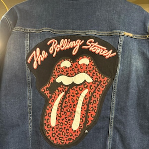 May include: A blue denim jacket with a black patch on the back. The patch features a red and black tongue with a leopard print design and the text "The Rolling Stones".