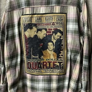 May include: A long-sleeved, button-down flannel shirt in a plaid pattern of pink, green, and white. The back features a graphic of the Million Dollar Quartet with Jerry Lee Lewis, Carl Perkins, Elvis Presley, and Johnny Cash.