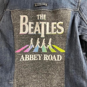 May include: A blue denim jacket with a gray patch on the back. The patch features a graphic of the Beatles with the text "The Beatles" and "Abbey Road".
