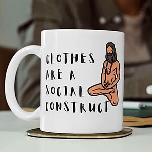 May include: White ceramic mug with the text "CLOTHES ARE A SOCIAL CONSTRUCT" and an illustration of a seated figure. The mug is on a coaster, with a blurred background.